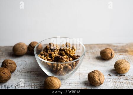 Walnut in a smale plate with scattered shelled nuts and whole nut which standing on a wooden vintage table. Walnuts is a healthy vegetarian protein Stock Photo