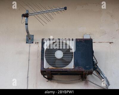 old air conditioner and tv antenna , rusty outdoor unit on a wall Stock Photo
