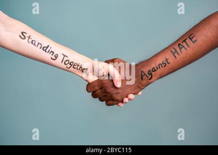 Handshake between black and white human woman and male hands with message text Standing Together against HATE. Concept of Black Lives Matter protest Stock Photo
