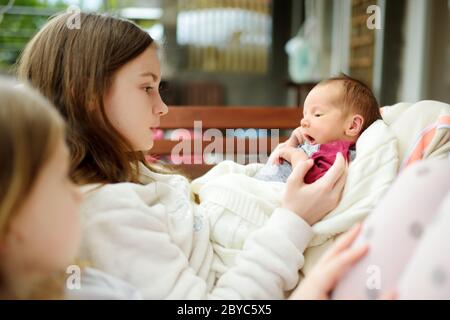 Two big sisters admiring their newborn brother. Two young girls holding their new baby boy. Kids with large age gap. Big age difference between siblin Stock Photo