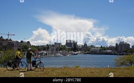 A pair of cyclists take in the view across the Inner Harbour in downtown Victoria, British Columbia, Canada on Vancouver Island looking towards the do Stock Photo
