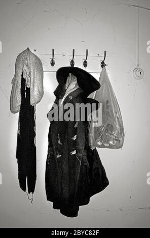 old coat, sweatshsirt and plastic bag, abandoned on vintage coat rack in disused building Stock Photo