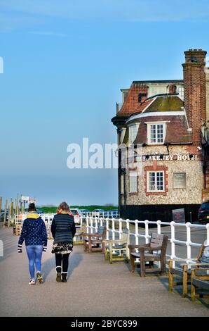 two  women walking past blakeney hotel on blakeney quay in warm late winter sunshiine Stock Photo