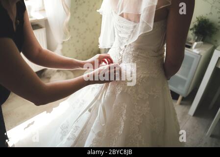 Close up of bridal corset. Rear view on bride in white wedding dress. Bridesmaid helping bride to dress wedding gown. Wedding day concept. Stock Photo