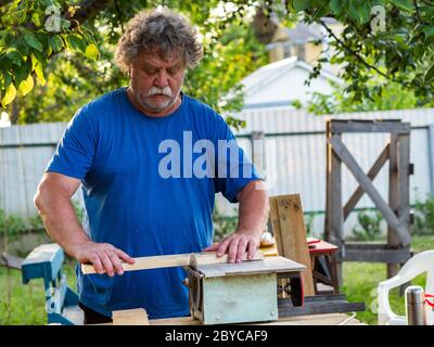 Caucasian Senior Male using circular saw for cutting wooden plank in the garden Stock Photo