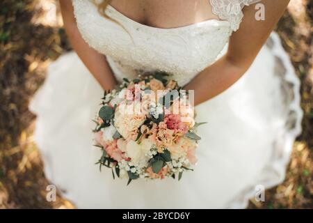Top view of bride holding colorful wedding bouquet in both hands. Outdoor photo. Shallow depth of field, focused on flowers. Wedding day concept. Stock Photo