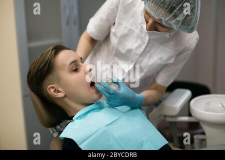 Female dentist puts on a guy patient a removable orthodontic teeth alignment in dental office. Stock Photo