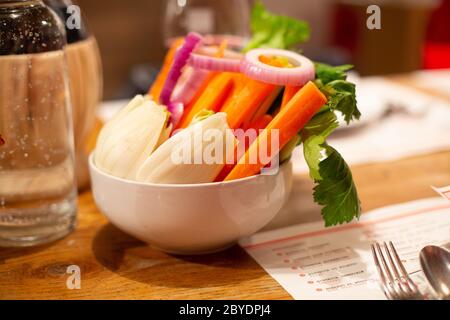 Vegan buddha bowl. Bowl with fresh raw vegetables - radish, carrot, ognion, radish, green parsley in a white ceramic plate on a wooden table. Hotel br Stock Photo