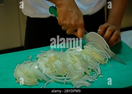 a chef slicing white onion on a green choping board Stock Photo