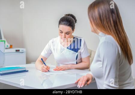 Young female doctor sits at her desk and chats to female patient while showing her test results Stock Photo