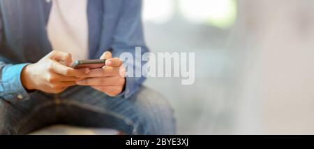 Close up view of a man using smartphone while sitting on sofa at hotel lobby with blurred background Stock Photo