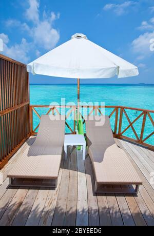 Parasol and chaise lounges on a terrace of water v Stock Photo