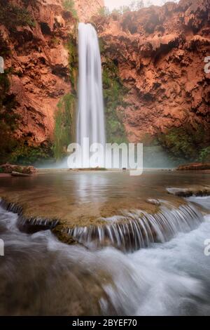 Beautiful turquoise water falls at Havasupai, in Arizona. Mooney Falls and red rock canyon wall. Stock Photo