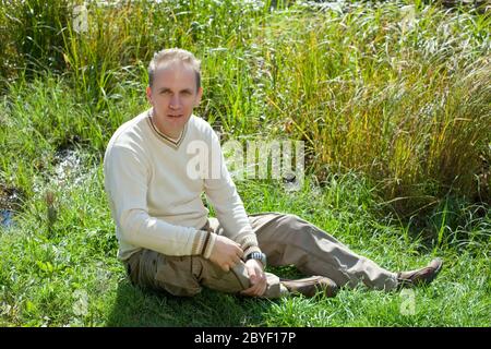 The man sits in a grass on the bank of the lake Stock Photo