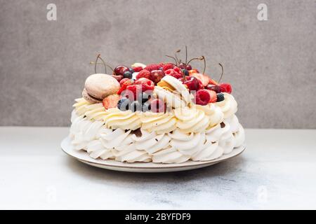 Big Pavlova meringue cake with fresh berries and macaroons on plain grey background. Copy space. Stock Photo