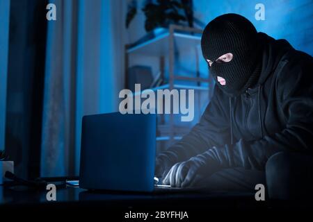 Masked hacker downloading private information using pc Stock Photo