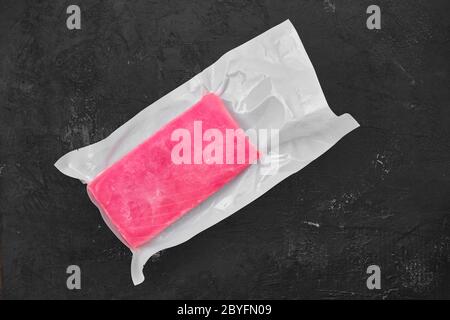 Raw frozen tuna fillet in vacuum packaging on black background Stock Photo