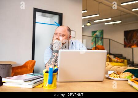 Bald tattooed man sitting at the table and looking thoughtful Stock Photo
