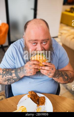 Bald man sitting at the table and eating a burger Stock Photo
