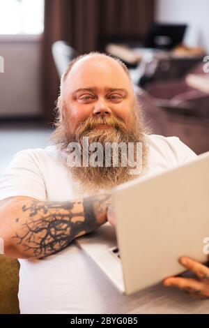 Bald bearded plump man sitting with a laptop in hands Stock Photo