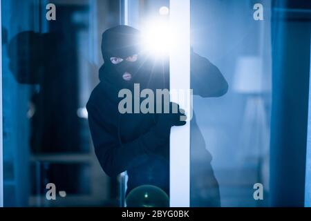 Thief breaking into apartment to steal, using torch Stock Photo