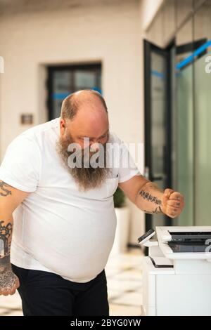 Bald bearded plus size man making copy on xerox and feeling angry Stock Photo