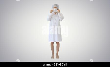 Wear the mask! Female doctor wearing a mask and pointing her finger up on gradient background. Stock Photo