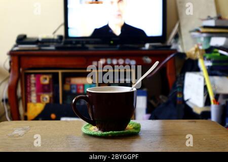 Photo of a coffee mug with a spoon on a table in front of a TV. Stock Photo