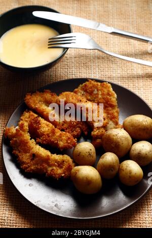 Photo of boiled potatoes and deep fried crispy fish strips on a plate. Stock Photo