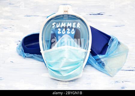 Text SUMMER 2020 written on a full face snorkel mask covered with a disposable surgical face mask lying on blue fins in protective shoe covers. Cancel Stock Photo