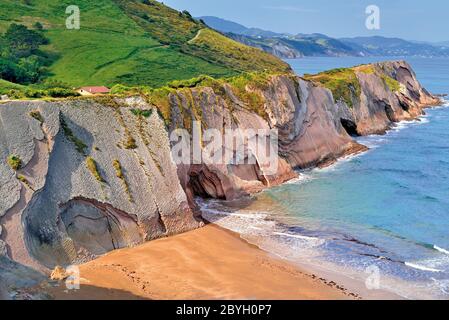 Great view of high rocky cliffs with green top, small chapel and sand beach at open ocean Stock Photo