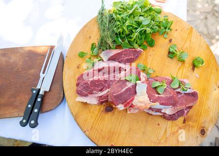Italy. Beef steaks on a cutting board waiting to be placed on the barbeque grill. Steaks with salad and steak knives. Stock Photo