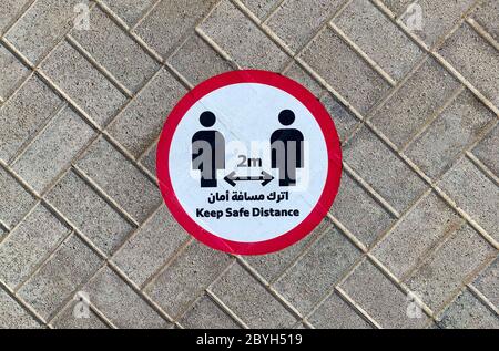 Dubai / UAE - June 10, 2020: 'Keep safe distance' sticker sign on a street pavement next to metro station in english and arabic languages. Social dist Stock Photo