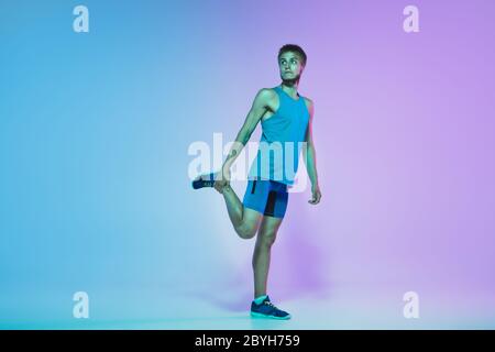 Portrait of active young caucasian man running, jogging on gradient studio background in neon light. Professional sportsman training in action and motion. Sport, wellness, activity, vitality concept. Stock Photo