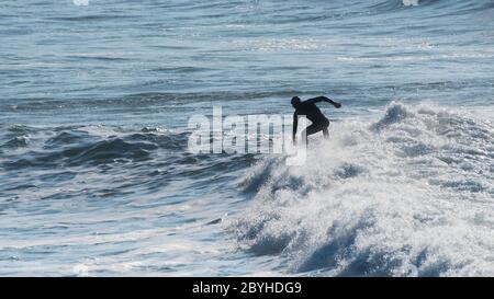 A panoramic image of the silhouette of surfer riding a wave  at Fistral in Newquay in Cornwall. Stock Photo