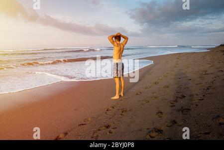 Image of fit man at workout running in morning along the beach. Jogging on along the seashore with beautiful orange sunrise over the sea in background Stock Photo