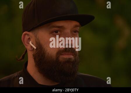 Man with a beard on a background of greenery.A guy with a black beard in a black baseball cap.The man is shot at sunset. Stock Photo