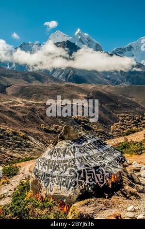 Nepal.Island Peak Trek. Buddhist mani stone prayer wall with the engraved Buddhist mantra of Om Mani Padmi Hum looking towards the peaks of Ama Dablam from above the Sherpa settlement of Dingboche Stock Photo