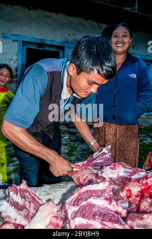 Nepal. Island Peak Trek. A visiting butcher demonstrates his skills to waiting Sherpa lady customers. Meat is a real treat for families in what is a basic vegetarian diet. The butcher has carried two whole leg loins of a Jak cow along the the animals liver from Lukla town several hours walk away visiting  all the small communities until there is nothing left of the meat. Even the bones will be used to make soup-broth then later pounded to dust to provide fertiliser Stock Photo