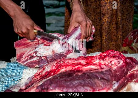 Nepal. Island Peak Trek. A visiting butcher demonstrates his skills to waiting Sherpa lady customers. Meat is a real treat for families in what is a basic vegetarian diet. The butcher has carried two whole leg loins of a Jak cow along the the animals liver from Lukla town several hours walk away visiting  all the small communities until there is nothing left of the meat. Even the bones will be used to make soup-broth then later pounded to dust to provide fertiliser Stock Photo