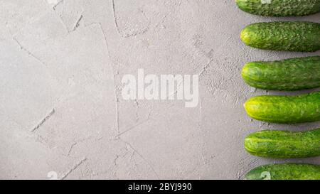 Line from cucumbers from right. Fresh green ripe cucumbers on gray concrete background. Gherkins on the table close-up. Stock Photo