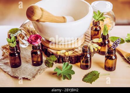 Using herbal essential oils in beauty products concept. Lot of various herbal oils with fresh plants on table above view. Vintage Instagram style filt Stock Photo