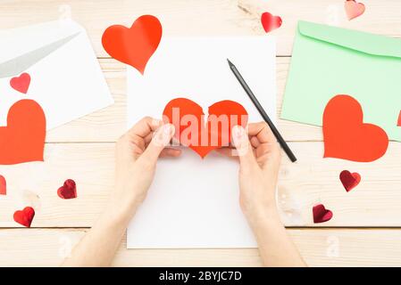 Woman's hands are holding a torn paper red heart. Loss of love, message, letter Stock Photo
