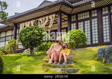 Mother and son travelers in medical mask stopped on the street and looking at the Japanese traditional building. Tourists travel in Japan after the Stock Photo