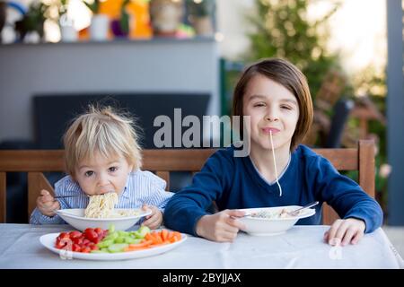 Cute children, boy brothers, eating spaghetti in garden summertime Stock Photo