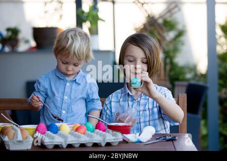 Sweet children, brothers, coloring and paiting eggs for Easter in garden, outdoors at home in backyard Stock Photo