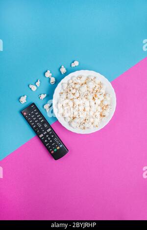 White bowl of popcorn on a blue and purple background with a black TV remote control Stock Photo