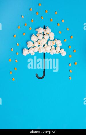 Umbrella and poruing rain drops made out of popcorn on a blue background Stock Photo