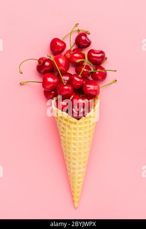 Fresh cherries in waffle cones Ice cream cone filled with fresh sweet cherry on pink background. Top view. Copy space. Summer creative concept Flat Stock Photo