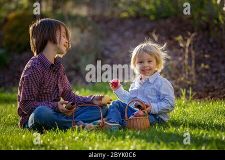 Cute children, eating chocolate bunnies and fighting with easter eggs after egg hunting in garden on sunset Stock Photo